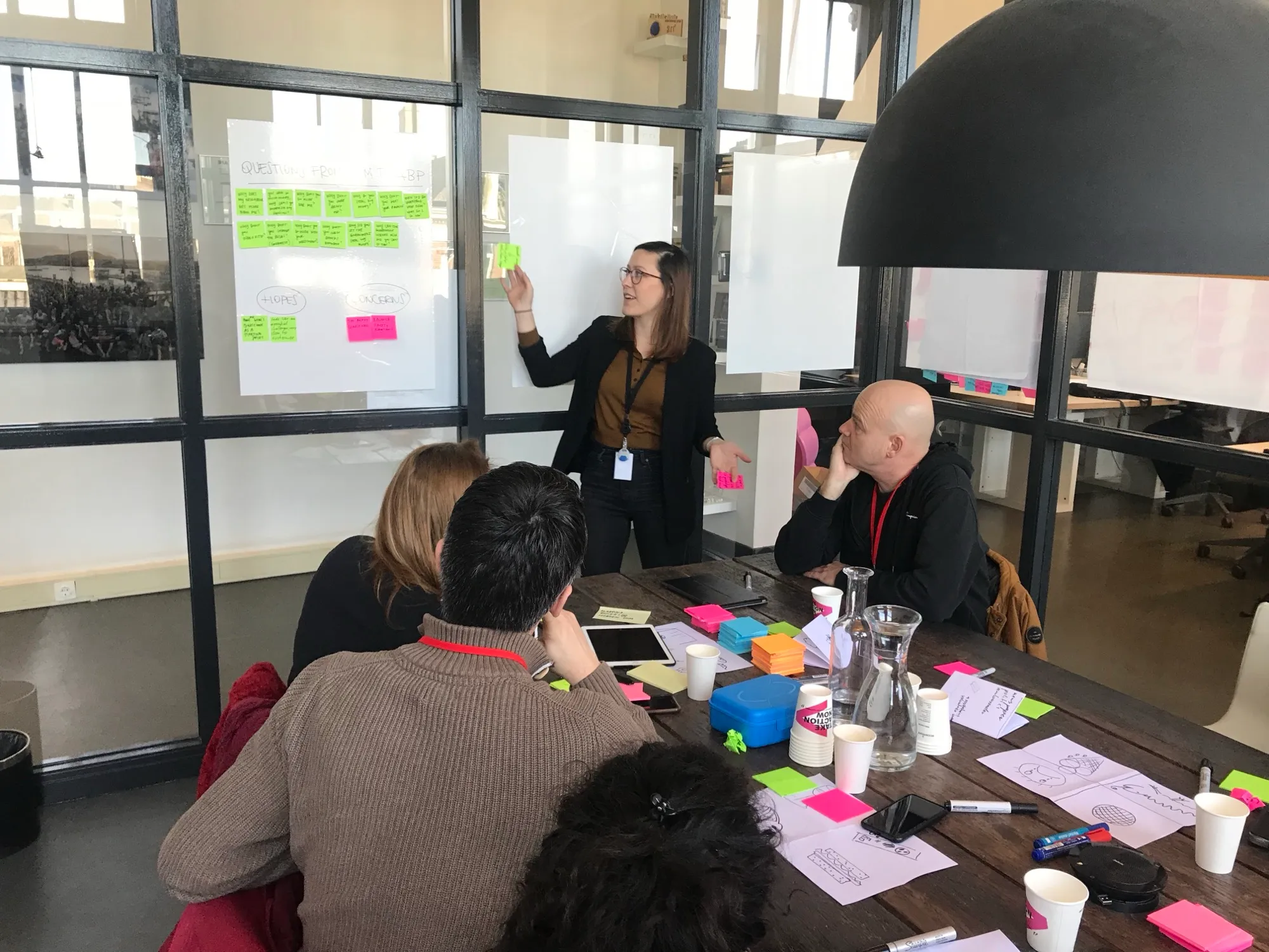 Kathrin at a whiteboard of sticky notes, running a discovery workshop with a team around the table